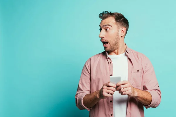 Chocado Bonito Homem Usando Smartphone Isolado Azul — Fotografia de Stock