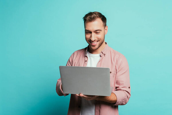 cheerful bearded man using laptop, isolated on blue