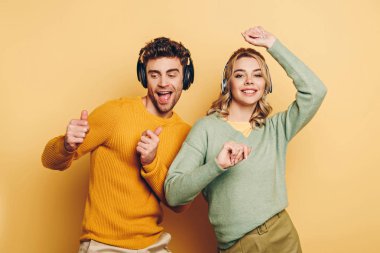 Mutlu çift sarı arka planda kablosuz kulaklıkla müzik dinlerken dans ediyor.
