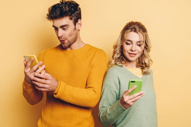 Olumlu, özenli çift sarı arka planda akıllı telefonlarda sohbet ediyor.