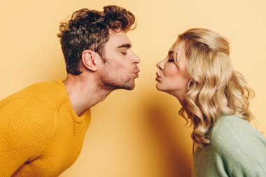 side view of man and woman kissing with closed eyes on yellow background clipart