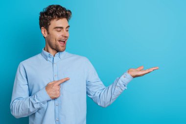 Neşeli genç adam mavi arka planda parmaklarını açık tutarak işaret ediyor.