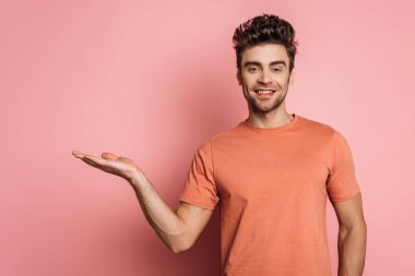 Mutlu genç adam pembe arka planda kolları açık dururken kameraya gülümsüyor.