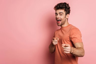 Heyecanlı genç adam kameraya bakıyor ve pembe arka planda parmaklarıyla işaret ediyor