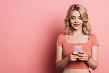Güzel, gülümseyen kız pembe arka planda akıllı telefondan sohbet ediyor.