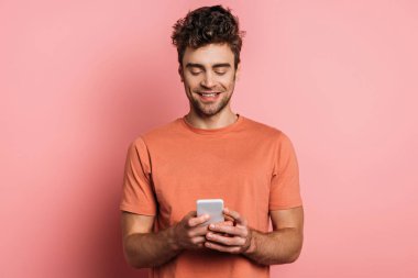 Gülümseyen genç adam pembe arka planda akıllı telefondan sohbet ediyor.