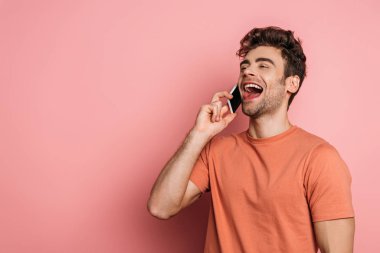 Pembe arka planda akıllı telefondan konuşurken gülen neşeli genç adam.