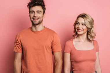 Güzel, neşeli kız pembe arka planda gülümseyen erkek arkadaşına bakıyor.