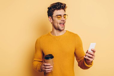 Neşeli adam sarı arka planda kahve içerken akıllı telefondan sohbet ediyor.