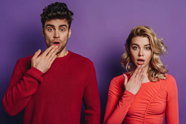 shocked man and woman looking at camera on purple background