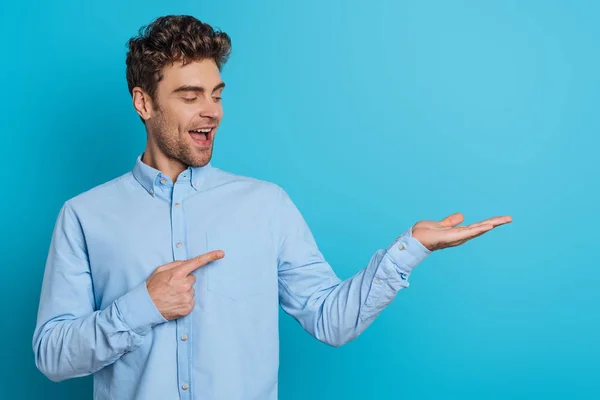 Cheerful Young Man Pointing Finger Open Arm Blue Background — 스톡 사진