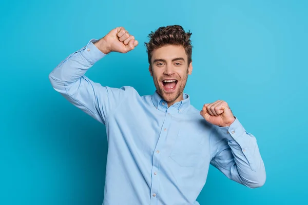 Vzrušený Mladý Muž Ukazuje Vítězný Gesto Při Úsměvu Kameru Modrém — Stock fotografie