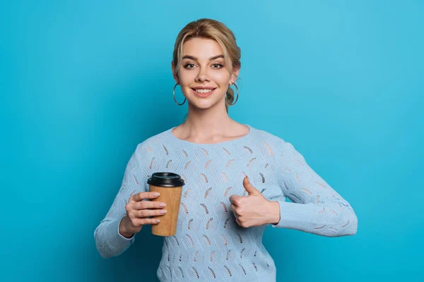 幸せそうな女の子がカメラで笑って親指を立ててコーヒーを持って青い背景に行く — ストック写真