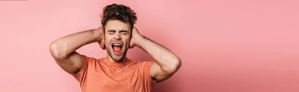 Panoramic Shot Irritated Young Man Shouting Covering Ears Hands Pink — Stock Photo, Image