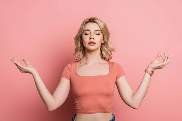 pretty girl meditating with closed eyes while standing on pink background