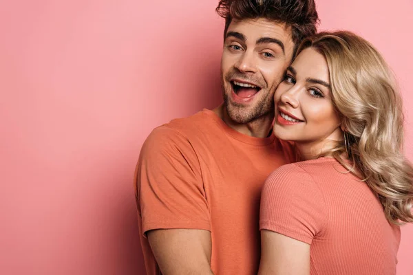 Feliz Jovem Casal Abraçando Enquanto Sorrindo Para Câmera Fundo Rosa — Fotografia de Stock