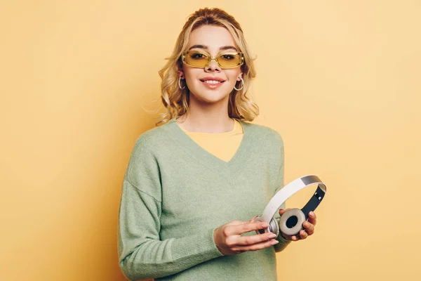 Bonita Chica Gafas Sosteniendo Auriculares Inalámbricos Sonriendo Cámara Sobre Fondo —  Fotos de Stock