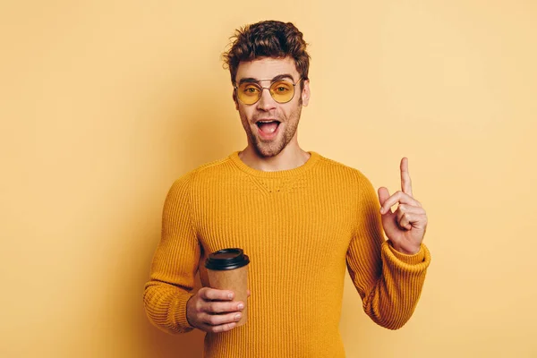 Aufgeregter Mann Zeigt Ideengeste Während Kaffee Auf Gelbem Hintergrund Hält — Stockfoto