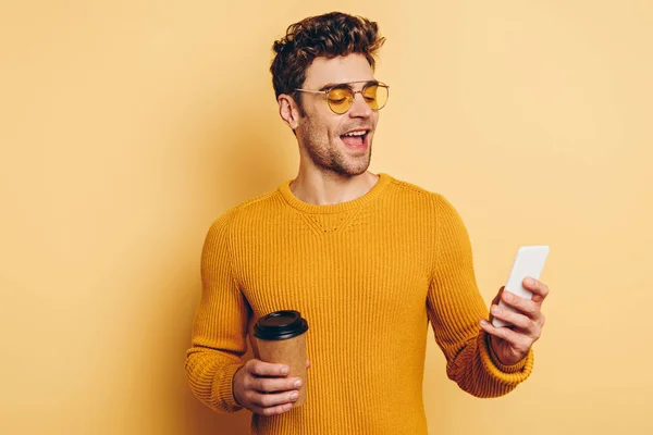 Wesoły Człowiek Czatujący Smartfonie Trzymając Kawę Żółtym Tle — Zdjęcie stockowe