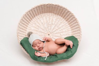 örgü şapkalı, beyaz sepetin içinde uyuyan, yeni doğmuş, melez bir bebek.