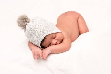 Örgü şapkalı melez bir bebek bembeyaz bir odada uyuyor. 