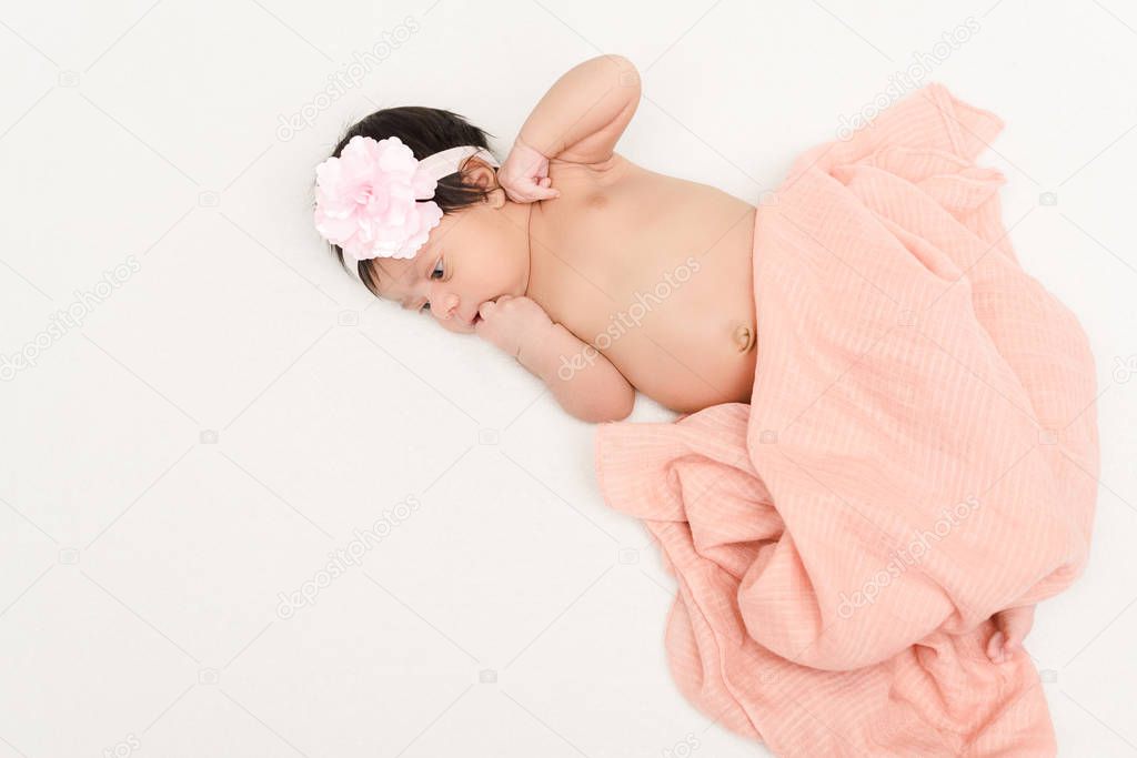 overhead view of bi-racial newborn baby in headband covered in blanket lying isolated on white 