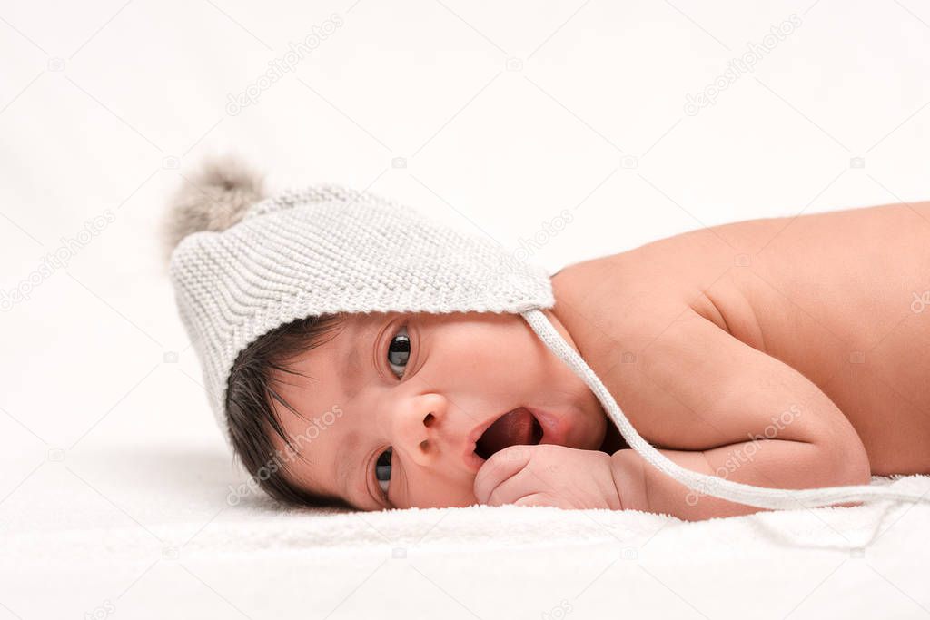 adorable bi-racial newborn baby in knitted hat lying on white 
