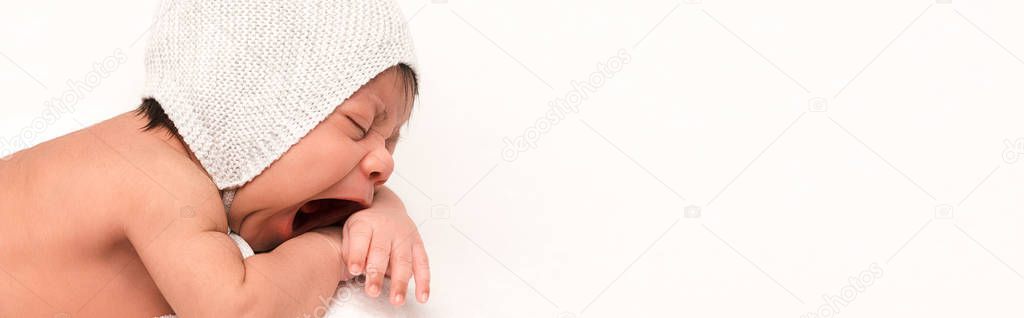panoramic shot of adorable mixed race baby in knitted hat yawning isolated on white 