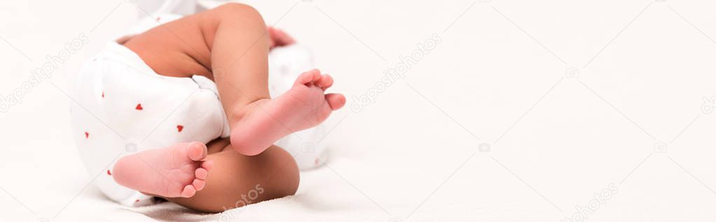 panoramic shot of newborn in baby romper lying on white 