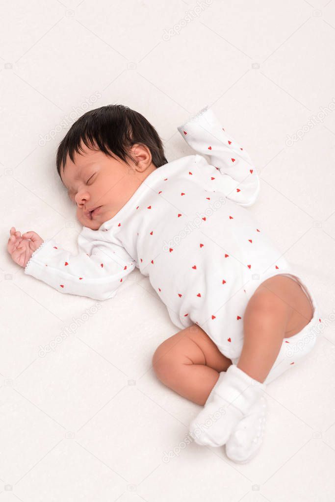 overhead view of bi-racial newborn in baby romper and socks sleeping isolated on white 
