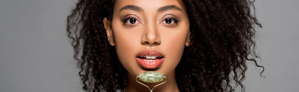 panoramic shot of african american girl using jade roller, isolated on grey
