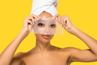 Kafasında havlu olan Afro-Amerikalı kız hidrojel maske takıyor, sarı üzerine izole edilmiş.