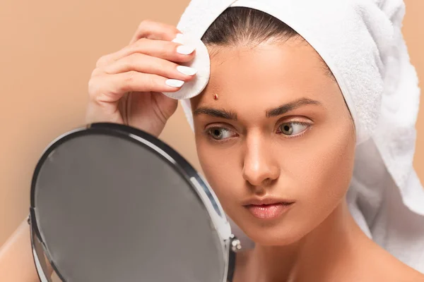 Young Woman Holding Cotton Pad While Looking Mirror Isolated Beige — 스톡 사진