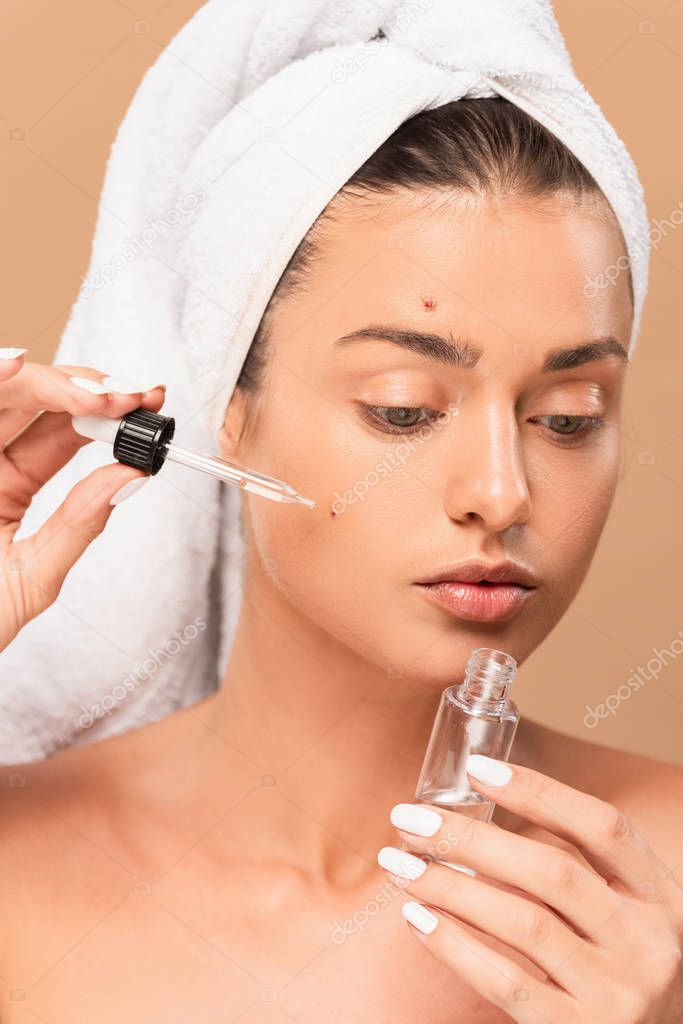naked woman applying serum on face with pimples isolated on beige 