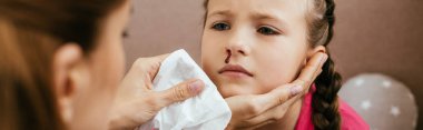 panoramic shot of mother holding napkin near upset daughter with nasal bleeding clipart