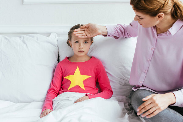 mother touching forehead of upset ill daughter with fever
