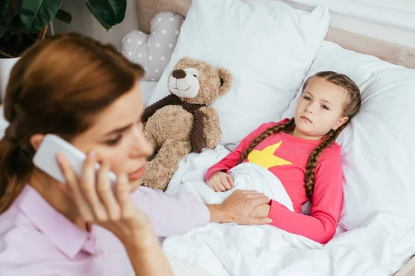 Visão Cortada Mãe Falando Smartphone Cama Com Filha Doente — Fotografia de Stock