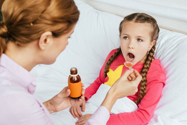 mother giving syrup to ill daughter in bed