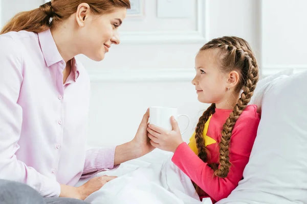 Smiling Mother Giving Hot Drink Sick Daughter Bed — Stock Photo, Image