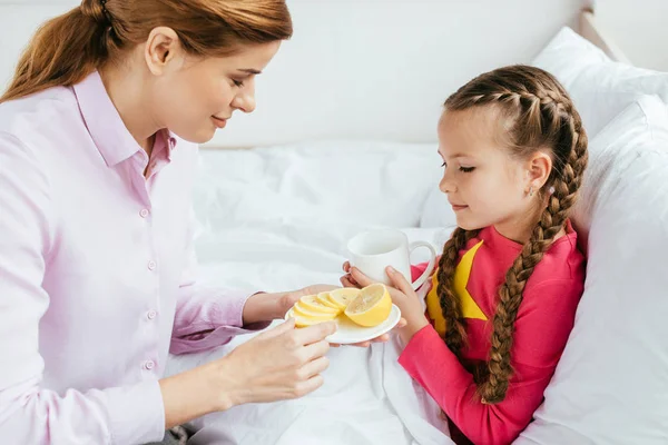 Smiling Mother Giving Lemon Ill Daughter Cup Hot Drink — Stock Photo, Image