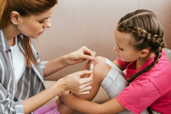 Madre Attraente Che Applica Intonaco Ginocchio Della Figlia — Foto Stock