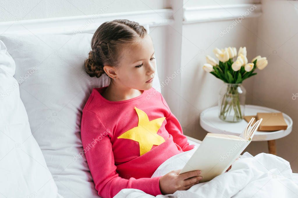child kid reading book while sitting on bed