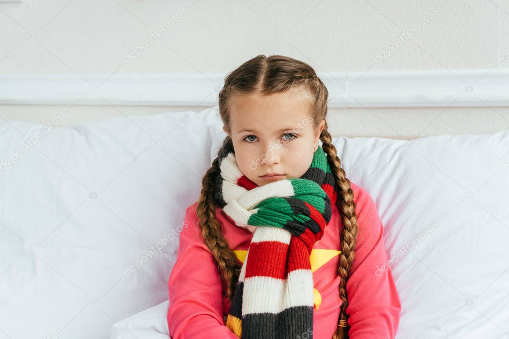 sad diseased kid in scarf sitting on bed