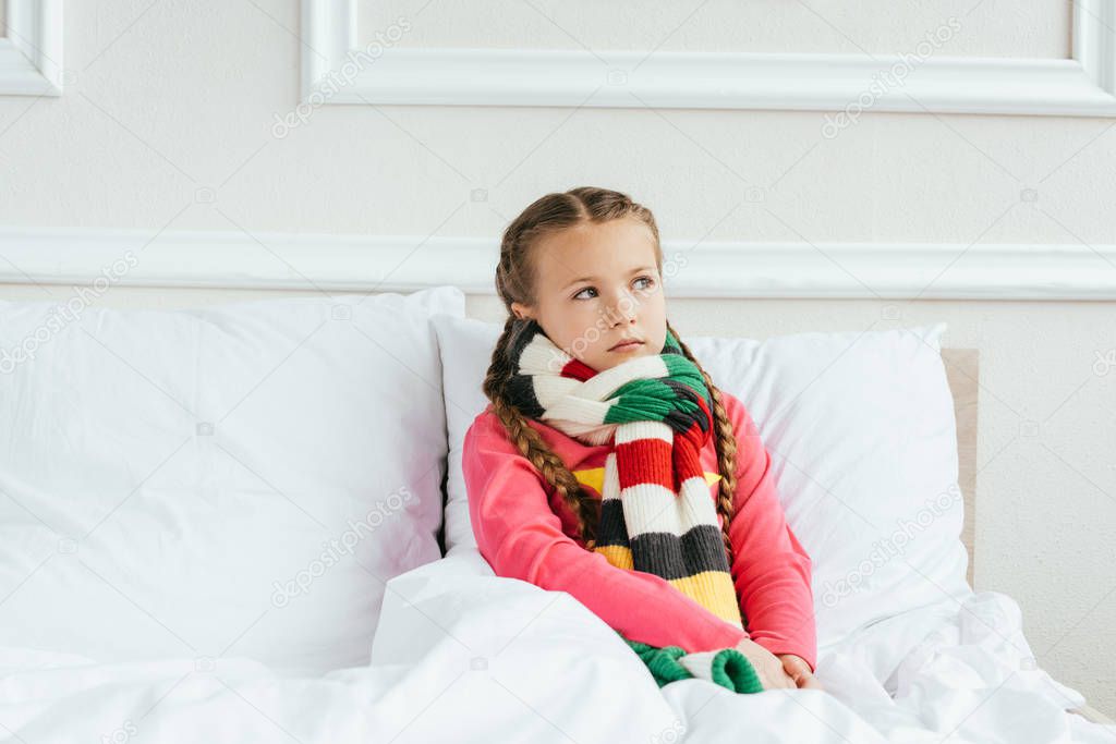 sad diseased child in scarf sitting on bed
