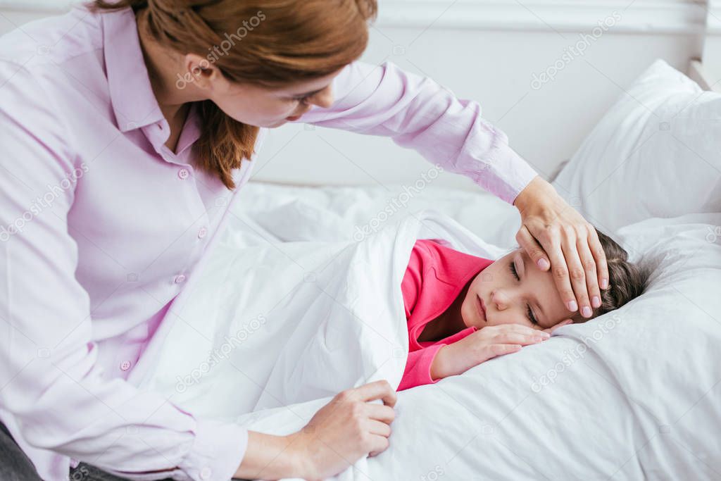 worried mother touching forehead of ill sleepy daughter with fever