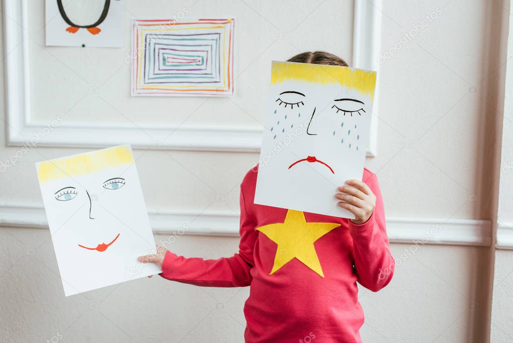 child holding two paintings with happy and sad faces