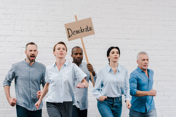 group of people walking near african american man holding placard with demokratie lettering 