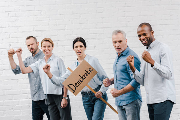 group of multicultural people standing near woman holding placard with demokratie lettering 