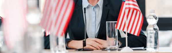 panoramic shot of businesswoman near american flags on table 
