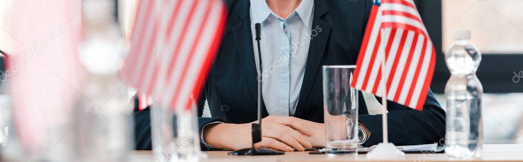 panoramic shot of businesswoman near american flags on table 